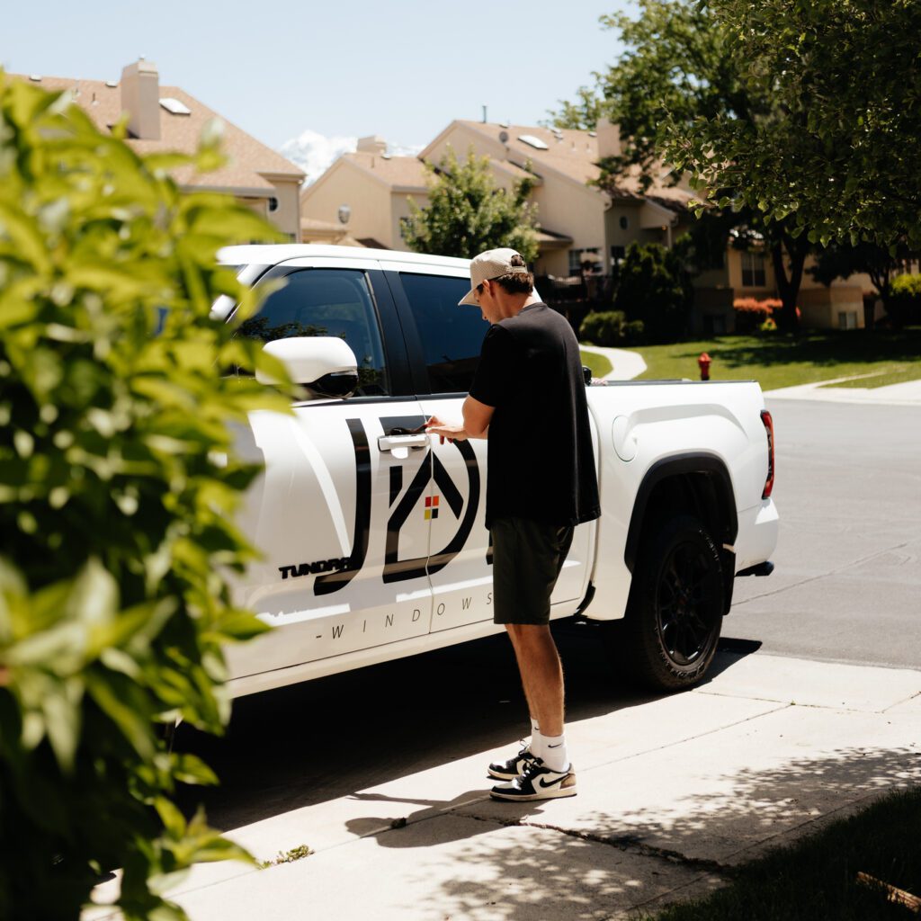 A man stands beside a white truck with the logo "JDI Windows" visible on the vehicle.