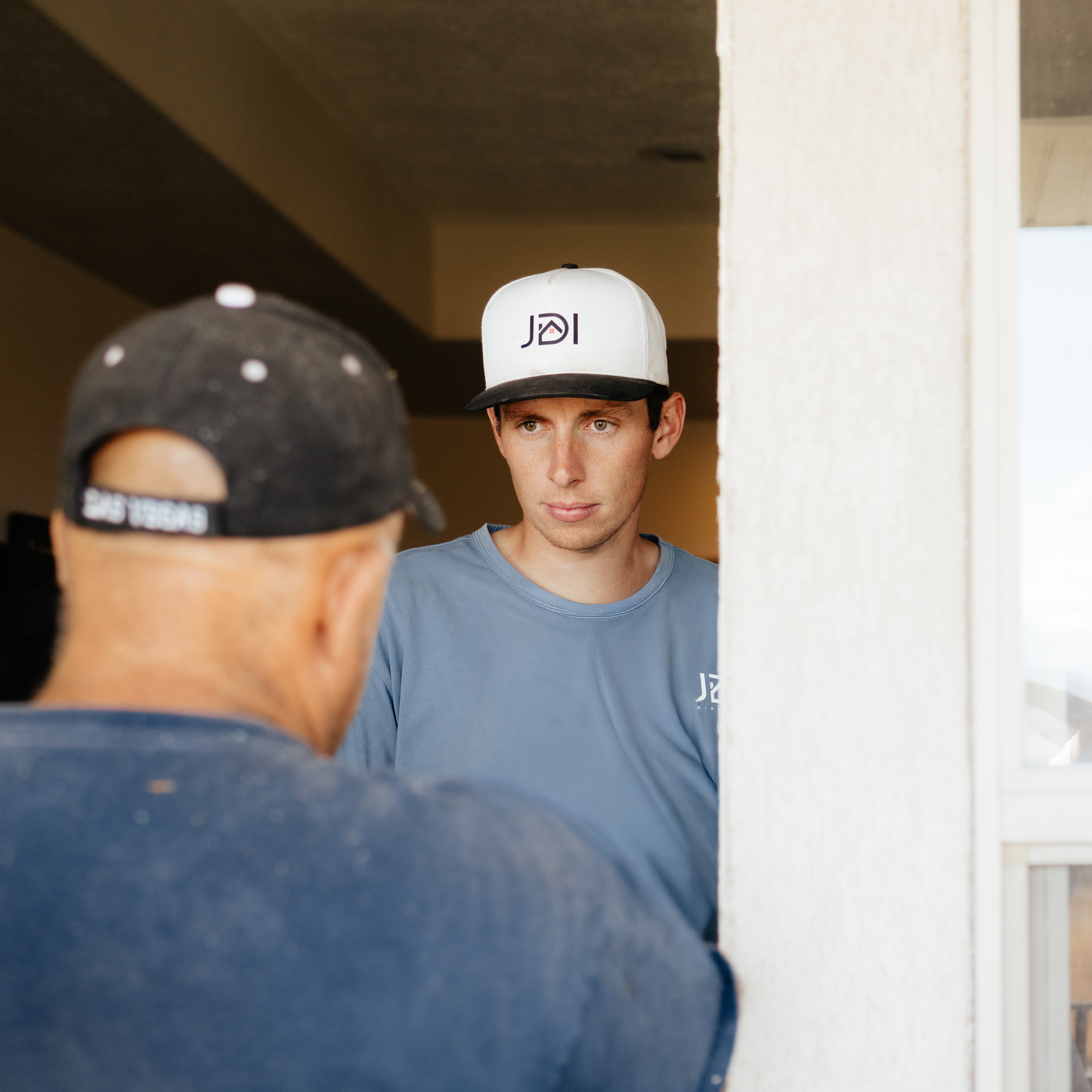 A man wearing a hat stands in front of a JDI Windows sign, showcasing a professional appearance.