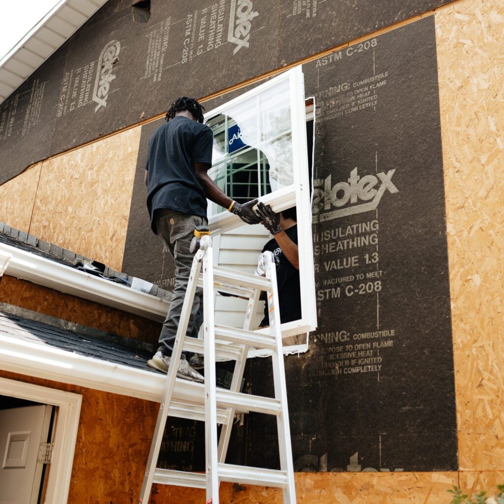 A man on a ladder working on a window installation for JDI Windows.