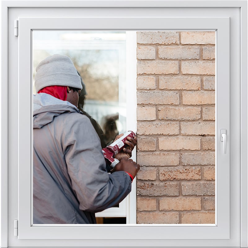 A man in a hoodie repairs a window, showcasing JDI Windows' services and expertise in home improvement.