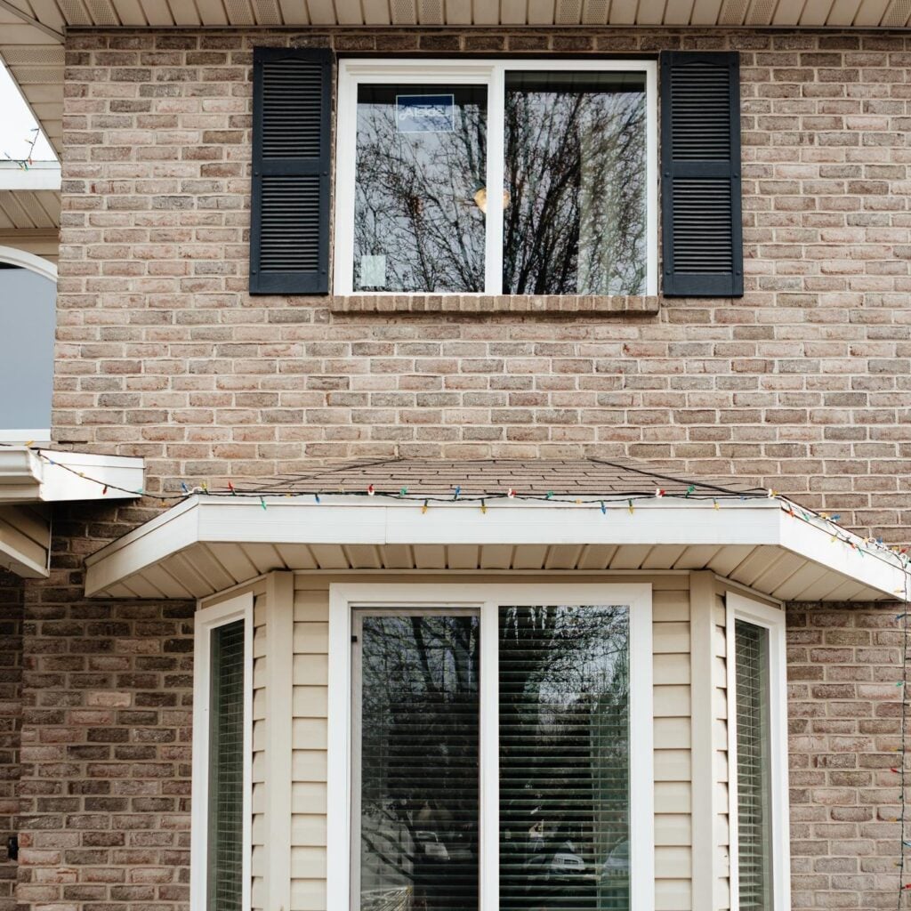 Two-story brick house facade with festive string lights along the roofline