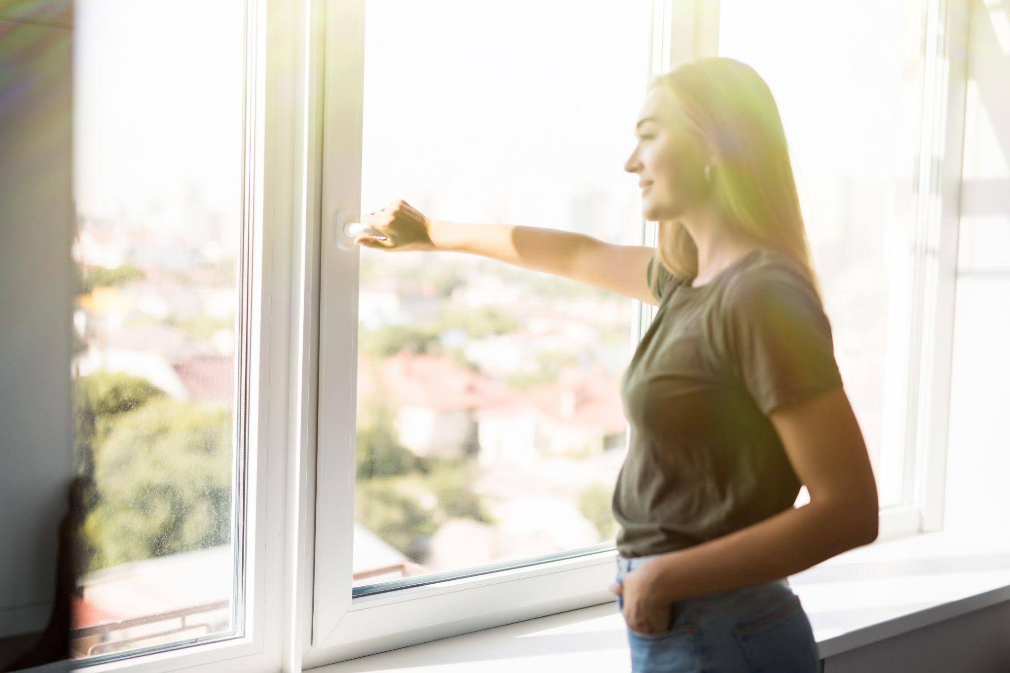 A woman stands by a window looking outside with a contemplative expression