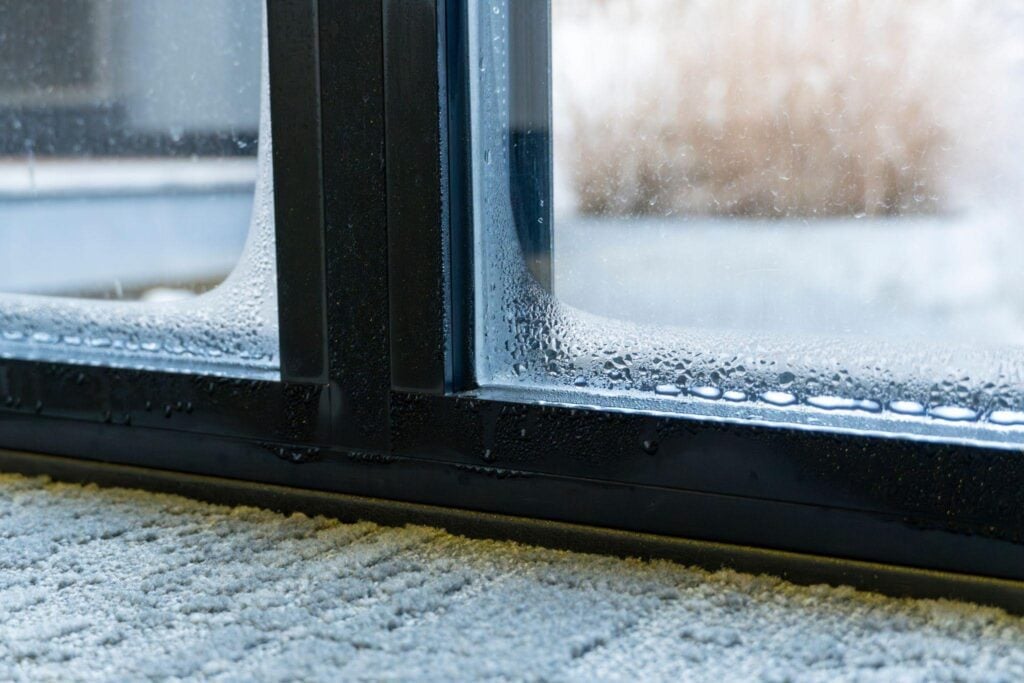 Close-up of a window pane covered in water droplets reflecting light and creating a blurred outdoor view