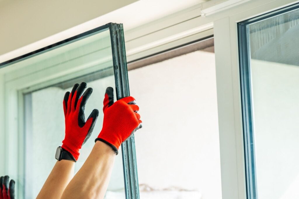A worker wearing red gloves installing a double-pane glass window.