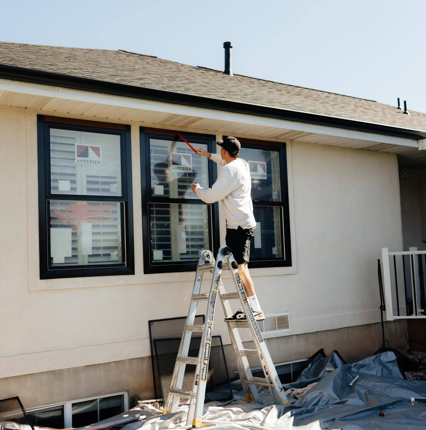 A man on a ladder painting the exterior of a house with a paintbrush and bucket